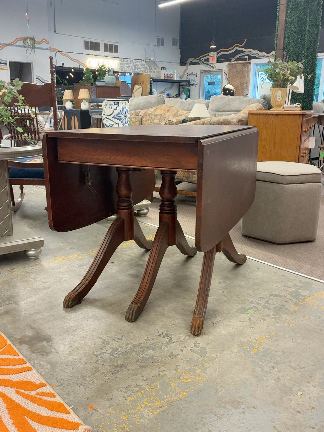 Dark brown Duncan Phyfe style drop-leaf table with double pedestals and visible finish wear
